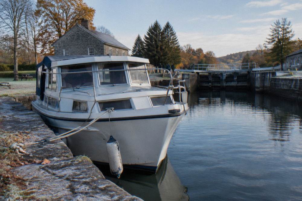 A rental canal boat tied up along a stone canal wall near a lock