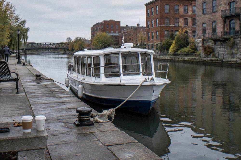 A cruise boat tied at a stone dock on the Erie Canal with old industrial buildings behind