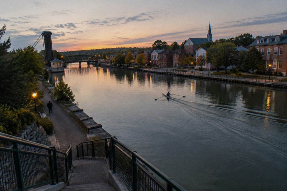 A wide canal basin at dusk with a village skyline and calm water in the foreground