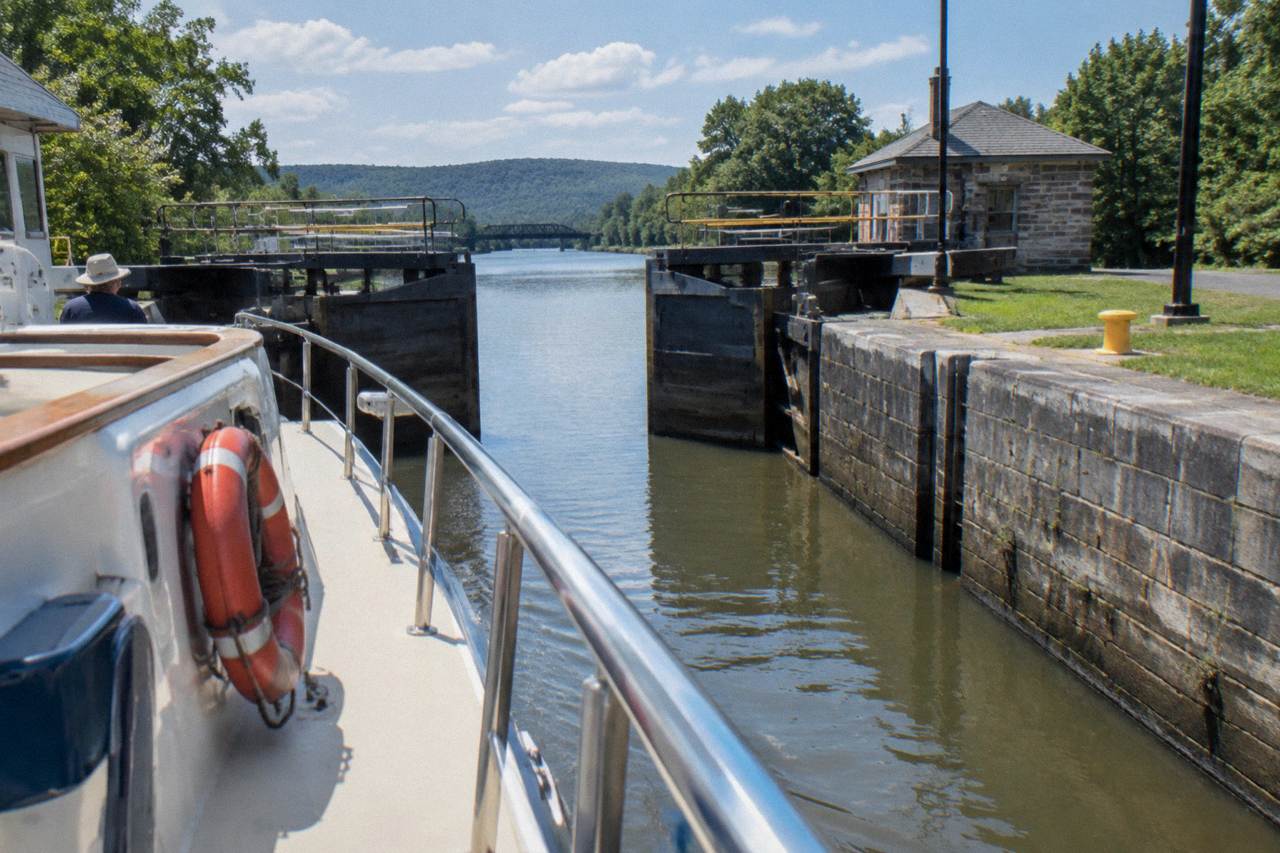 A canal cruise boat passing through a set of Erie Canal lock gates on a calm afternoon