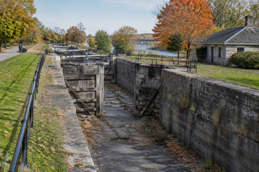 Stone lock walls and wooden gates of the restored Flight of Five locks beside the modern canal in Lockport