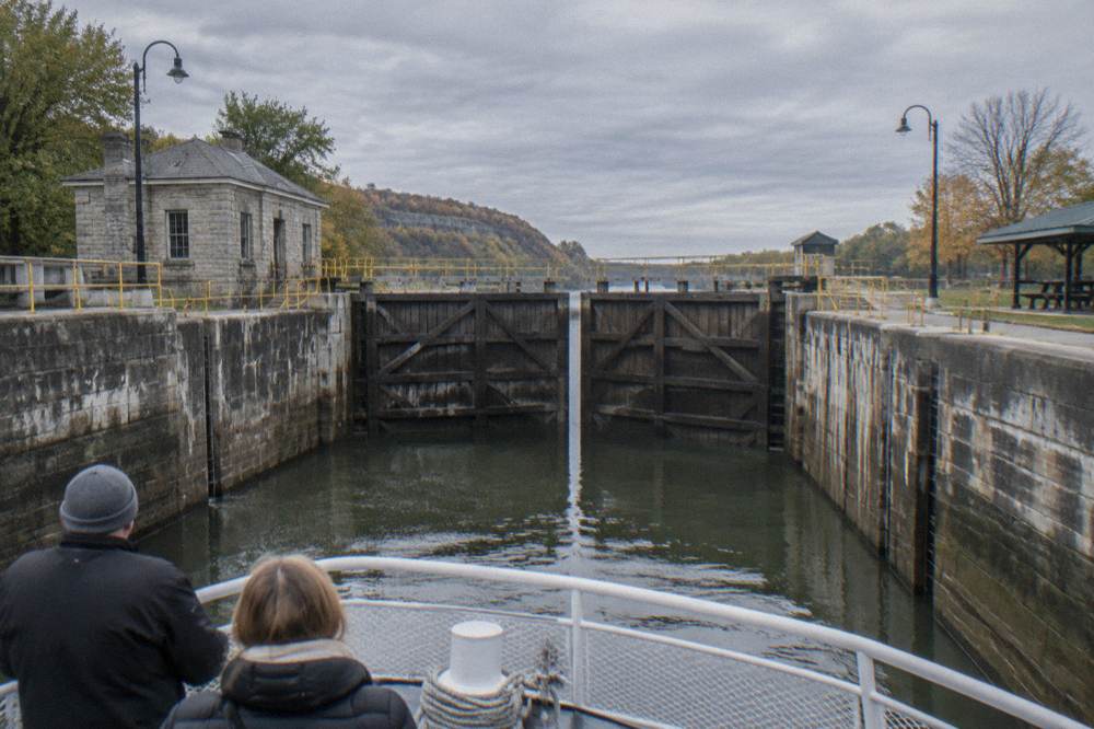 A lock chamber viewed from a boat deck with tall timber gates and a stone wall rising above the waterline