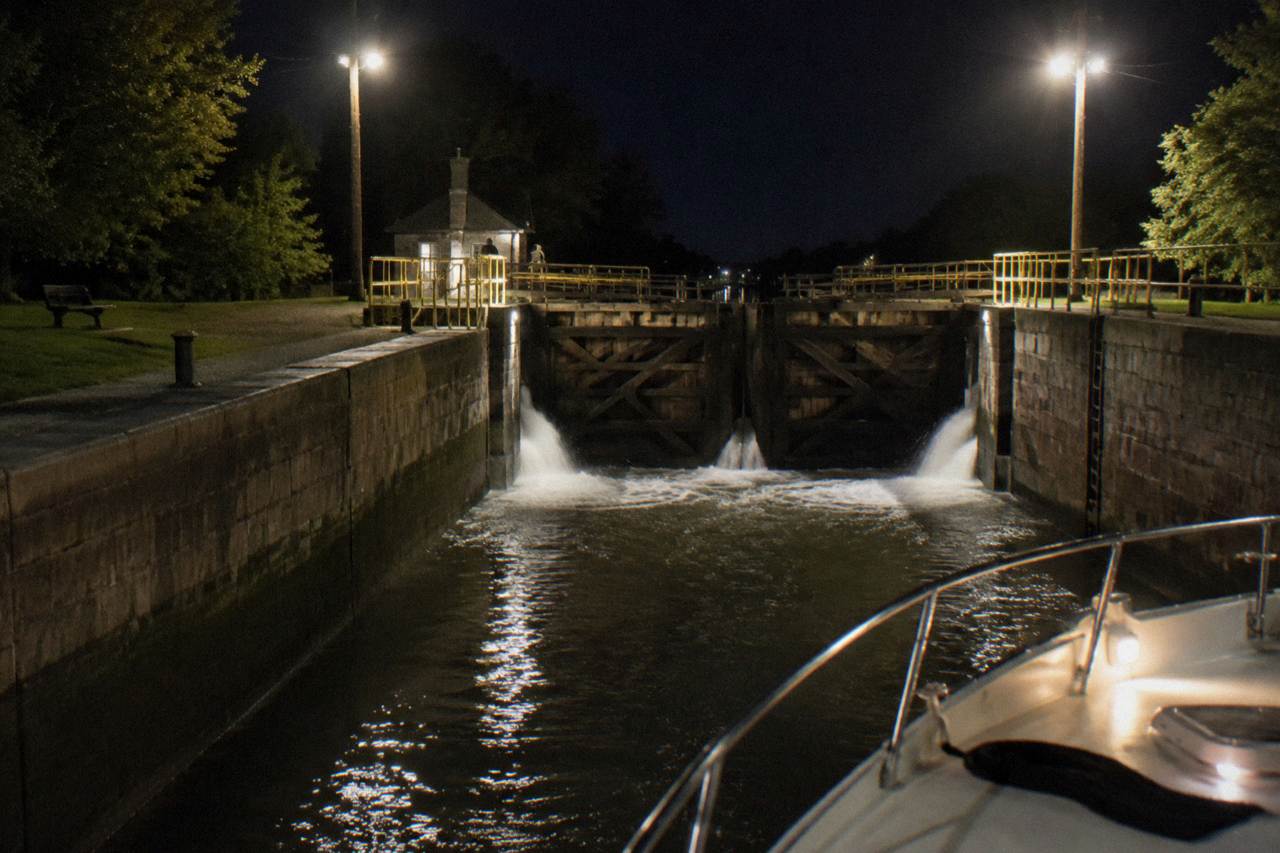 A canal boat passing through a stone lock chamber with wooden gate doors and water pouring through the valves