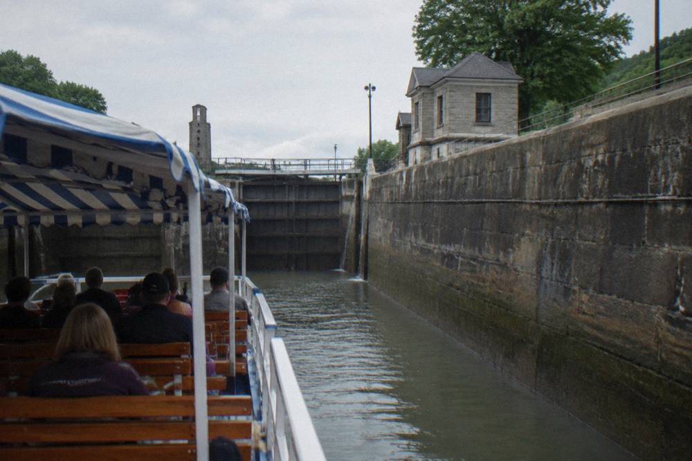 A narrated cruise boat passing through an Erie Canal lock with passengers seated on open decks