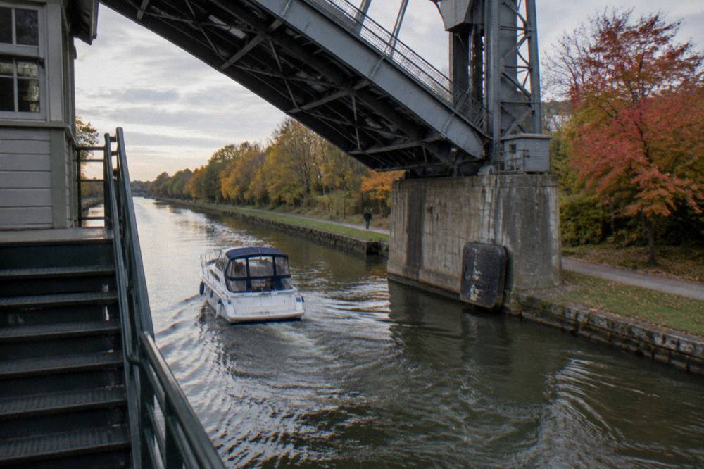 A canal boat underway past trees showing early fall color along the towpath