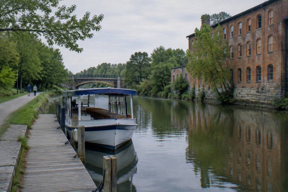 A quiet canal dock in late spring with a tour boat tied up and few people on the towpath