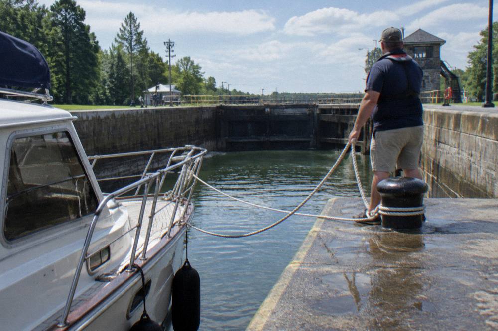 A skipper holding a lock rope as a canal boat waits inside a lock chamber