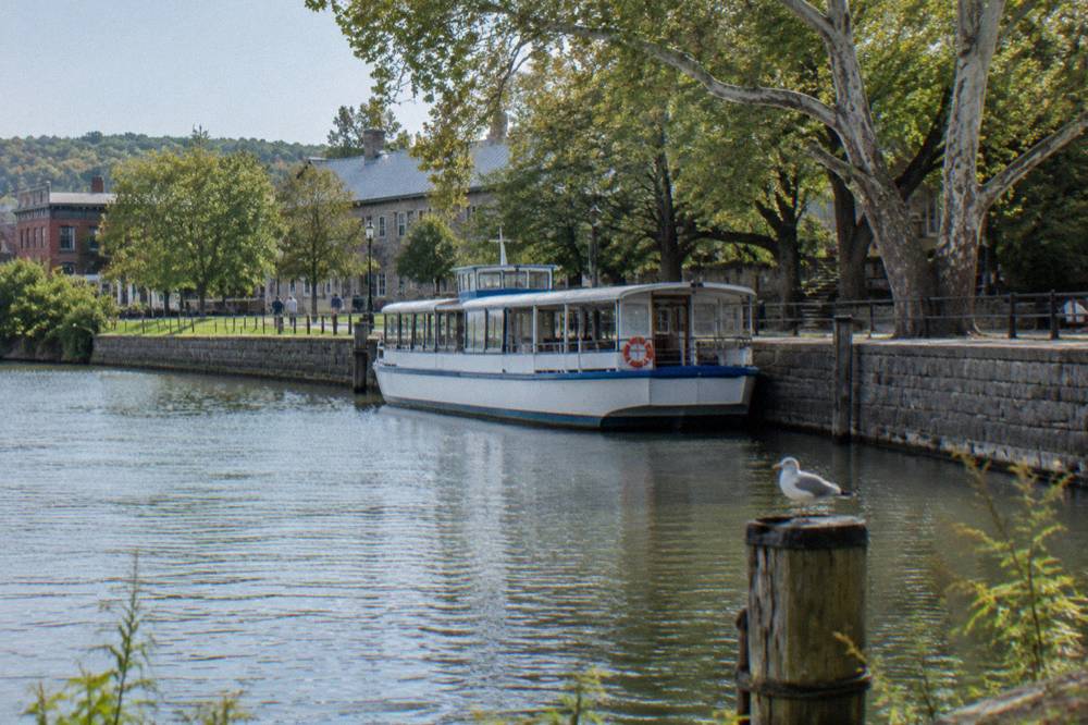 A canal dock with a passenger boat tied up beside a stone embankment and trees