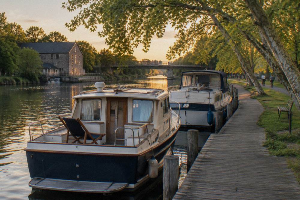 Two canal boats tied side by side at a wooden dock on a tree-lined canal
