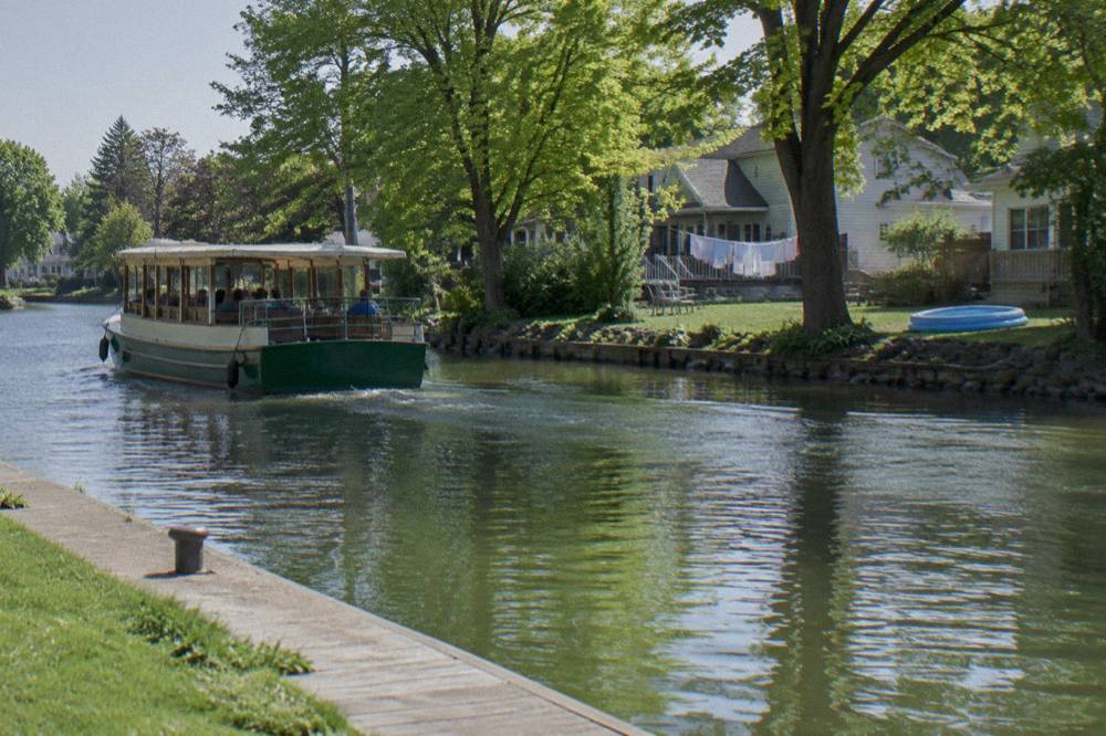 A canal tour boat cruising past tree-lined banks and backyards along the Erie Canal