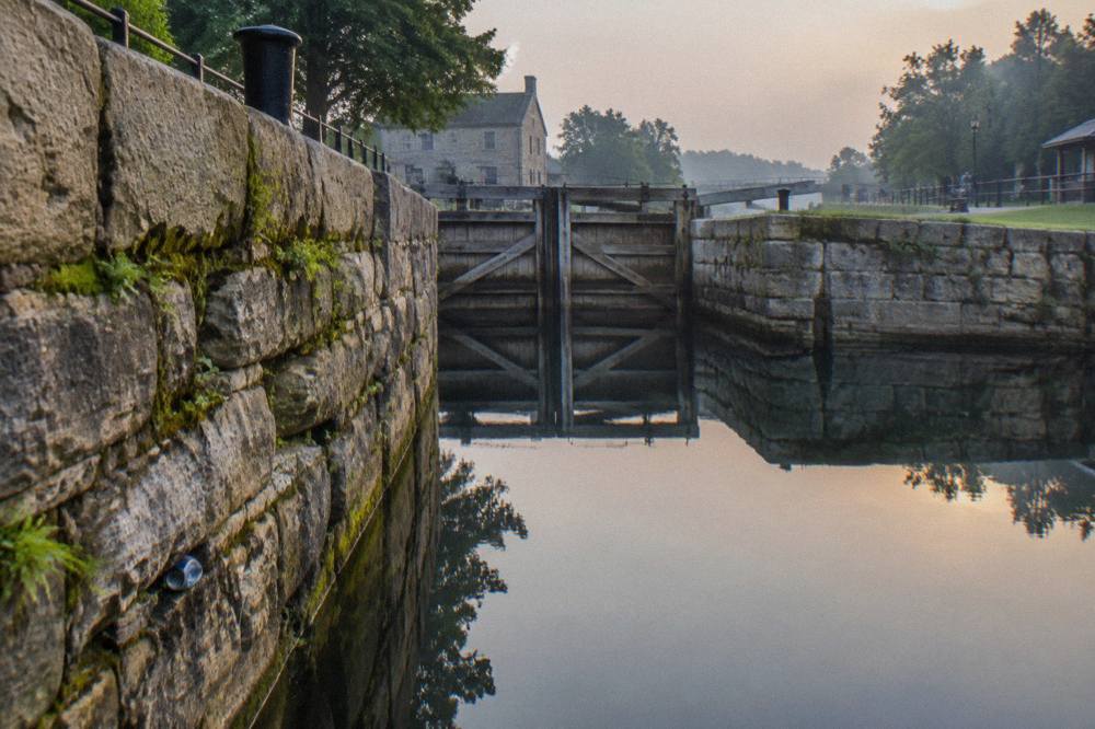 A restored stone lock wall along the Erie Canal with wooden gates reflected in still water