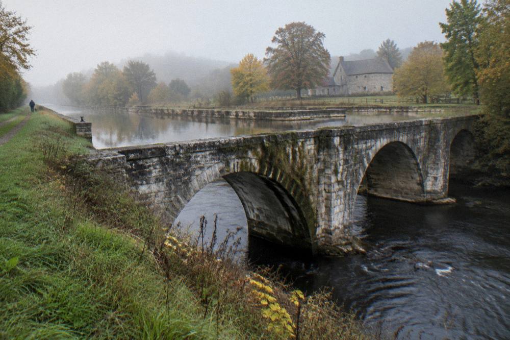 A stone aqueduct arch carrying water over a river along the old canal line