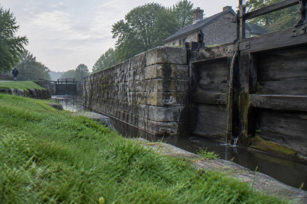 A stone lock wall and wooden gate on the Erie Canal beside a grassy bank