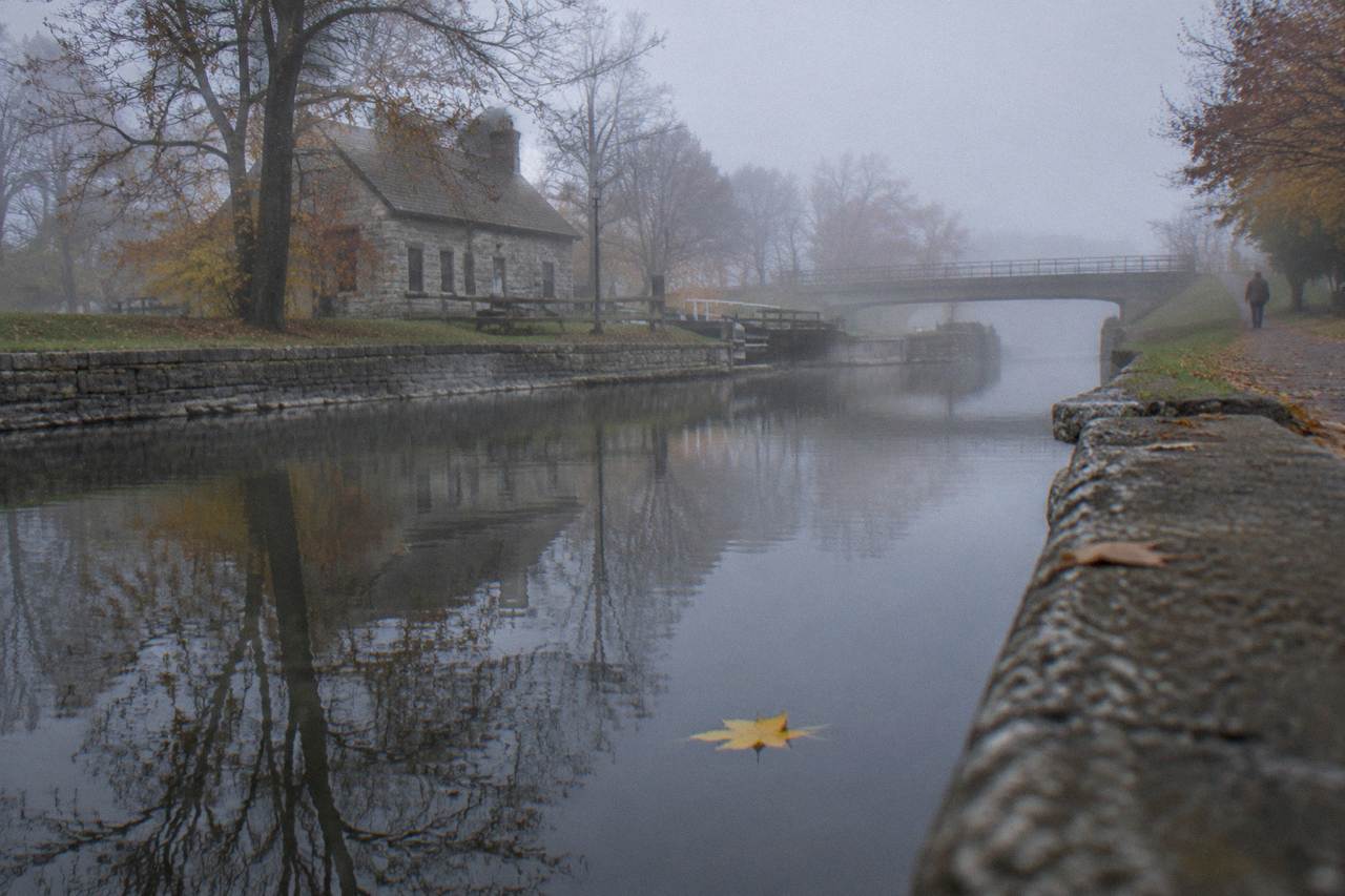 Calm canal water reflecting autumn trees along a stone-edged Erie Canal channel