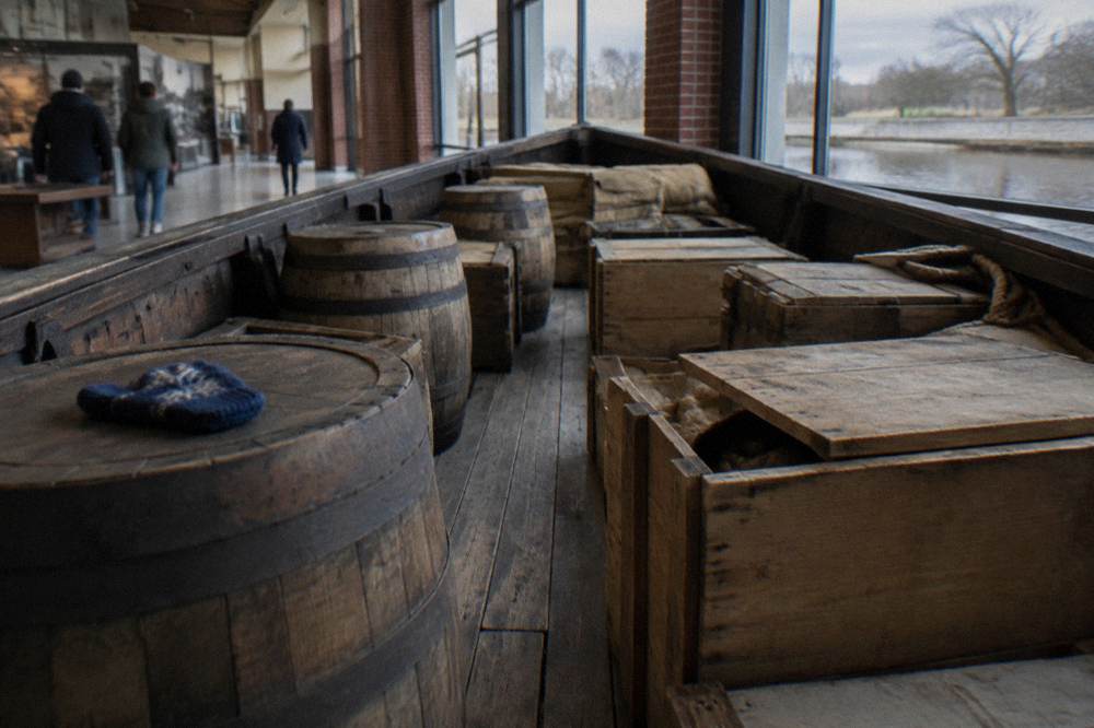 A walk-through canal boat hull displayed inside a museum gallery with period cargo crates
