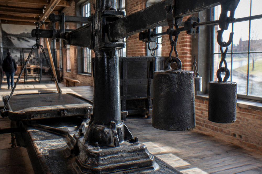 A historic weighlock scale and machinery displayed in a brick museum interior