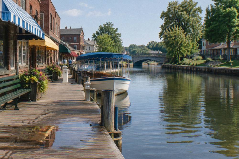 Canal village main street with shops and benches beside the water and a boat at the dock