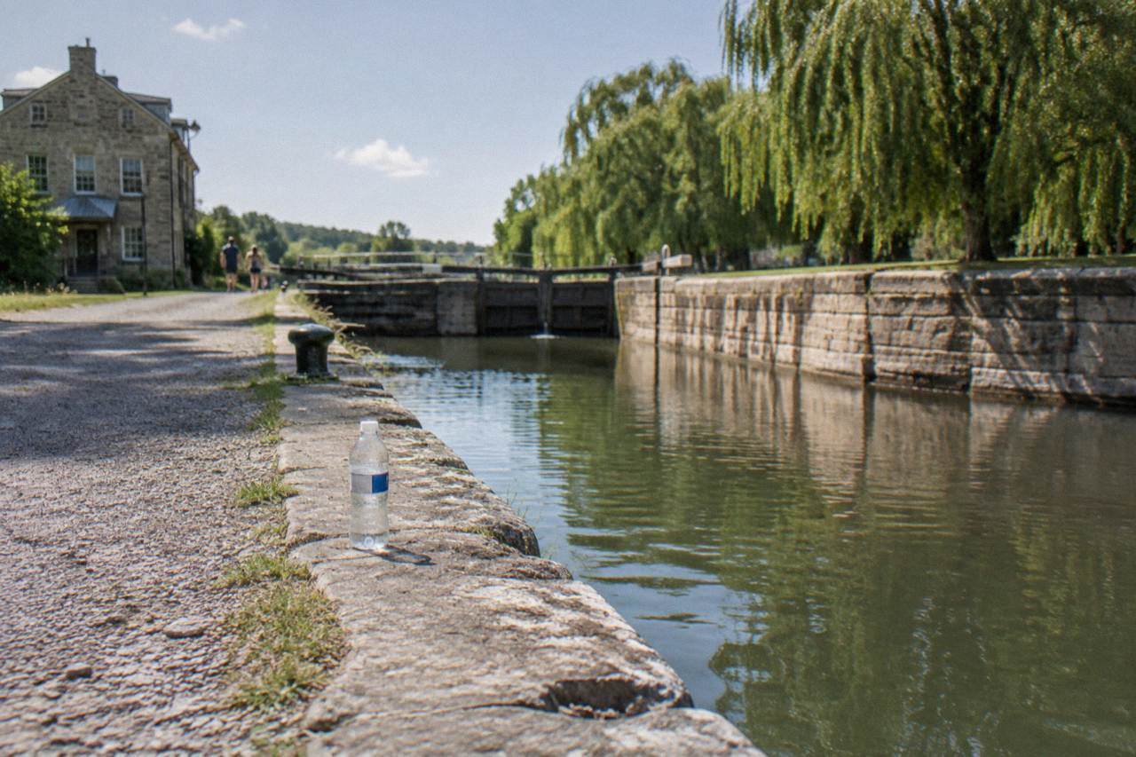 Towpath trail beside a calm canal with a stone lock wall and trees along the far bank