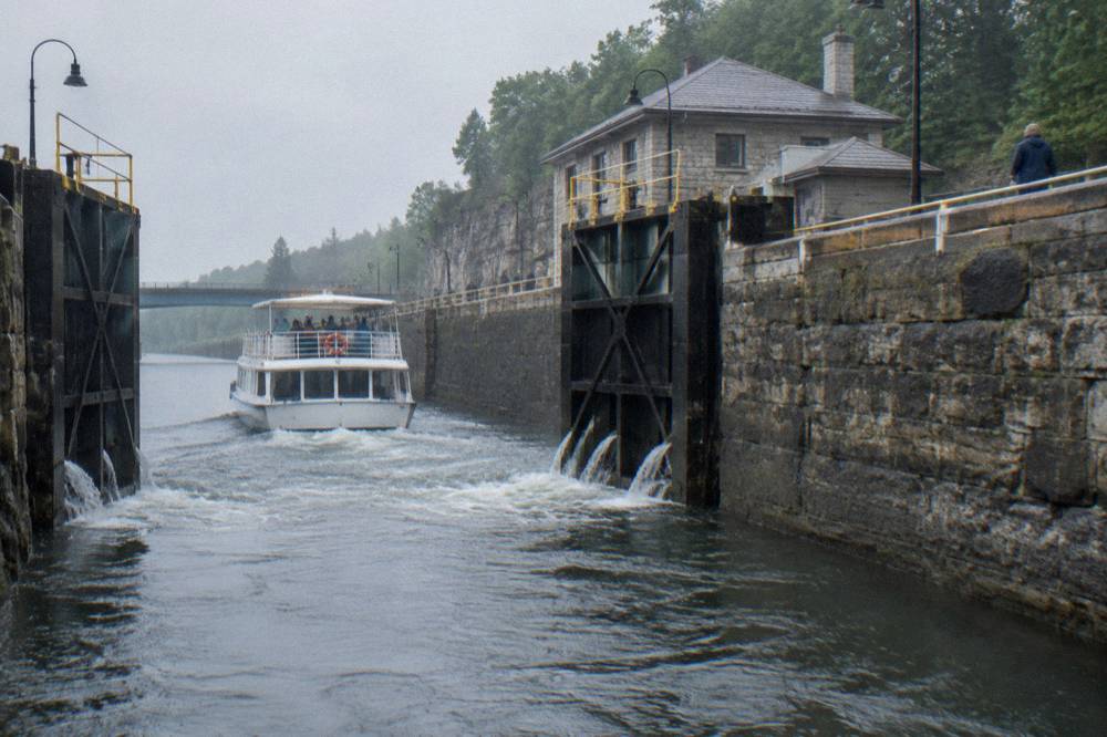 A small cruise boat passing through open lock gates with water pouring from the gates