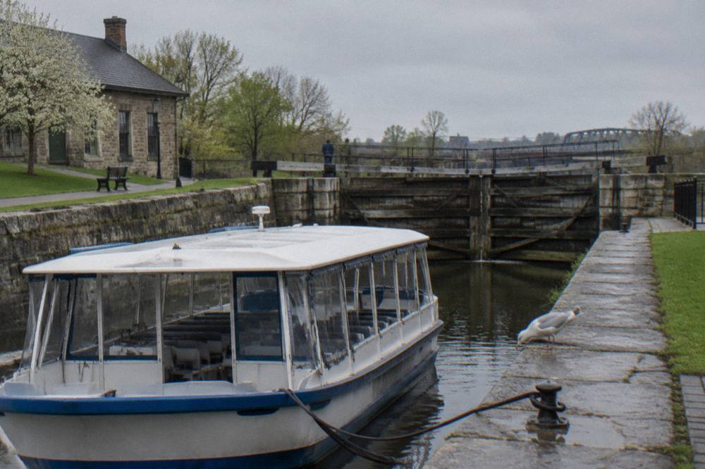 A tour boat tied at a stone canal dock with old wooden lock gates in the background