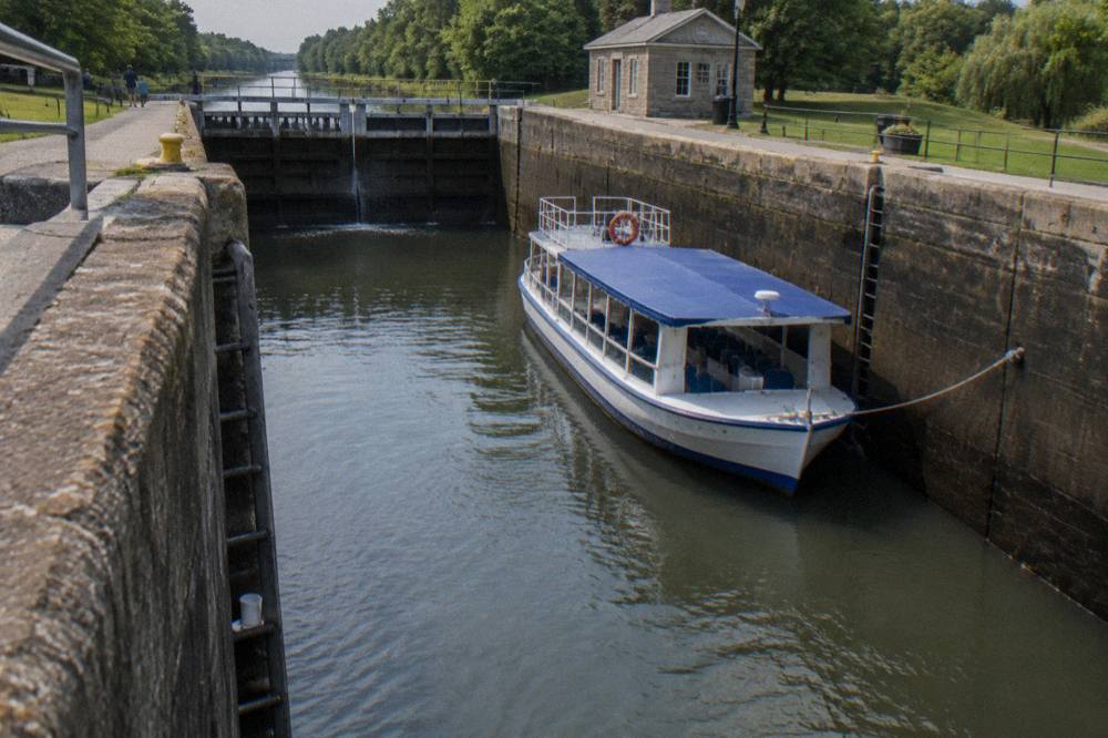 A passenger cruise boat tied up inside a canal lock with tall stone walls rising on both sides
