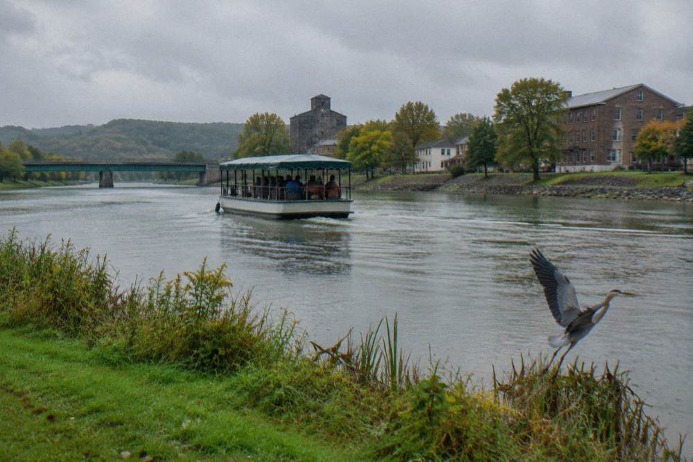 A covered canal cruise boat moving along a wide river stretch with green banks