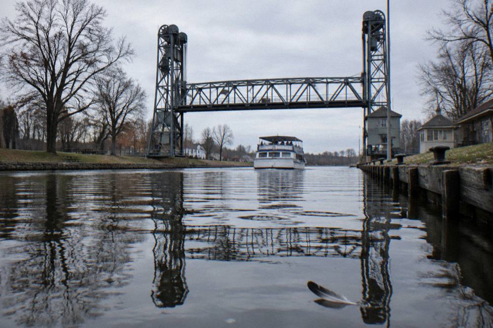 A small cruise boat passing under a canal lift bridge on calm flat water
